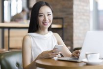 Chinese woman working with laptop and smartphone in cafe — Stock Photo