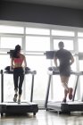 Jovem casal exercitando em esteiras na academia — Fotografia de Stock