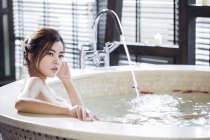 Young Chinese woman filling bathtub with rose petals — Stock Photo
