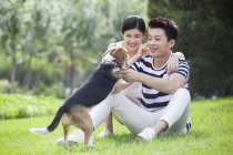 Cinese coppia giocare con carino beagle in parco — Foto stock