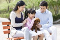 Азиатская семья сидит на скамейке в парке с собакой — стоковое фото