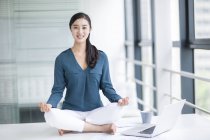 Chinese woman meditating on office desk — Stock Photo