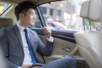 Hombre de negocios chino sentado en el asiento trasero del coche con teléfono inteligente - foto de stock