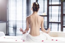 Vista trasera de una joven meditando envuelta en una toalla - foto de stock