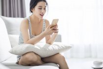 Asiatico donna utilizzando smartphone su divano in casa interno — Foto stock