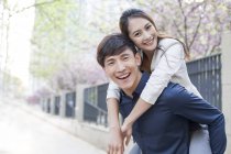 Chinese man piggybacking girlfriend on street — Stock Photo