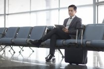 Азиатский мужчина ждет в аэропорту и с помощью цифрового планшета — стоковое фото