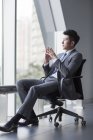 Chinese businessman sitting in chait and looking through window — Stock Photo