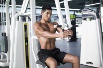 Chinese man exercising at gym equipment — Stock Photo