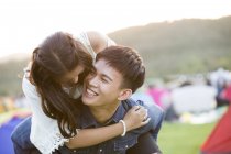 Happy chinese couple riding piggyback at festival camping — Stock Photo