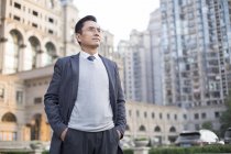 Chinesischer Geschäftsmann mit den Händen in den Taschen schaut in der Stadt weg — Stockfoto