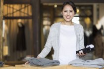 Владелец китайского магазина одежды стоит рядом с считывателем кредитных карт — стоковое фото