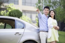 Китайська пара вказуючи і, спираючись на автомобіль — стокове фото