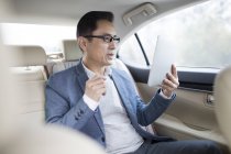 Азиатский мужчина с цифровым планшетом на заднем сидении автомобиля — стоковое фото
