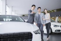 Revendeur de voitures montrant des voitures au couple chinois dans la salle d'exposition — Photo de stock