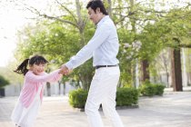 Asian father and daughter spinning around in park — Stock Photo