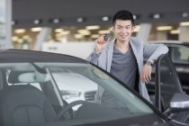 Man holding keys to new car in showroom — Stock Photo