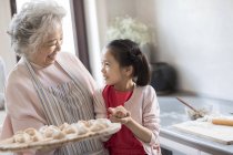 Nieta y abuela chinas haciendo albóndigas en la cocina - foto de stock