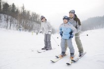 Padres chinos enseñando a hijo a esquiar en estación de esquí - foto de stock