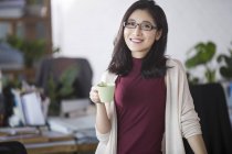 Young asian office worker standing with cup in office — Stock Photo
