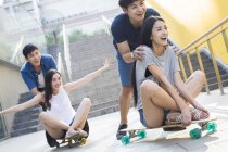Chinese men pushing girlfriends on skateboards — Stock Photo