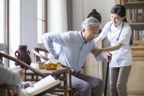 Chinese nursing assistant taking care of senior man in room with tea — Stock Photo