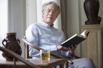 Senior Chinese man reading book in living room — Stock Photo