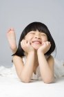 Kleines chinesisches Mädchen liegt vorne auf grauem Hintergrund — Stockfoto