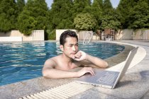 Uomo cinese che utilizza il computer portatile a bordo piscina resort — Foto stock