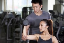 Trainer helping Chinese woman lifting dumbbell — Stock Photo