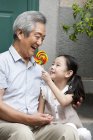 Chinese grandfather and granddaughter sitting with lollipop on porch — Stock Photo