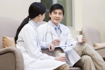 Médicos chinos hablando en el hospital con café - foto de stock