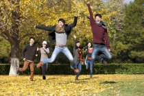 Chinese young adults jumping on lawn in autumnal park — Stock Photo