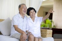 Senior Chinese couple sitting on sofa at resort and pointing — Stock Photo