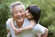Chinese girl embracing grandfather from behind in garden — Stock Photo