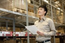 Trabajador de almacén chino con portapapeles mirando hacia arriba - foto de stock