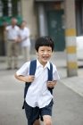 Chinese schoolboy running on street with grandparents in background — Stock Photo