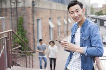 Chinese hält Smartphone auf Straße und schaut in Kamera — Stockfoto