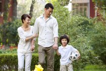 Chinese parents walking in city garden with son with soccer ball — Stock Photo
