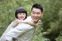 Chinese father giving daughter piggyback ride in garden — Stock Photo