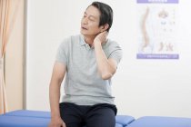 Paciente chino mayor sosteniendo su doloroso cuello - foto de stock
