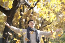 Chinese man enjoying falling autumn leaves in park — Stock Photo