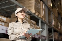 Chinese warehouse worker with clipboard looking up — Stock Photo