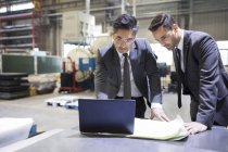 Businessman and engineer using laptop at factory — Stock Photo
