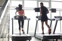 Couple chinois faisant de l'exercice sur tapis roulants en salle de gym — Photo de stock