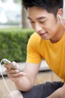 Chinese man and in earphones using smartphone — Stock Photo