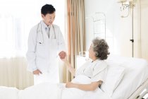 Médico chino cogido de la mano con paciente en el hospital - foto de stock