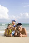 Молодая семья в масках для подводного плавания лежит на пляже — стоковое фото