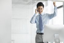 Веселый китайский бизнесмен разговаривает по телефону в офисе — стоковое фото