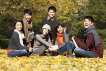 Chinese young adults sitting on lawn in autumnal park — Stock Photo